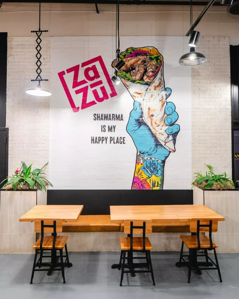 A wall mural of the Zazu logo and and a hand holding a shawarma 